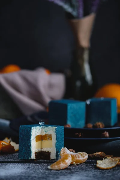 Pastel azul lleno de naranja y mandarina en forma de cubo. Cerca en una mesa negra hay ingredientes naranjas, mandarinas, nueces. Estilo rústico Imagen de archivo