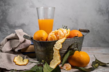 Konteynırda yaprakları olan birkaç mandalina beyaz bir masanın üzerinde, arka planda hafif bir zemine uzanır. Rustik biçim kopyalama uzayı.