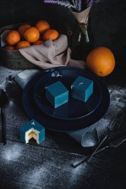 Küp şeklinde portakal ve mandalinayla dolu mavi pasta. Siyah bir masanın üzerinde portakal, mandalina ve fındık var. Kırsal biçim