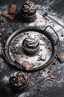 Birkaç kek ya da siyah masada çikolata şekilli kremalı kekler. Pudra şekeri keklerin üzerine saçılmış..
