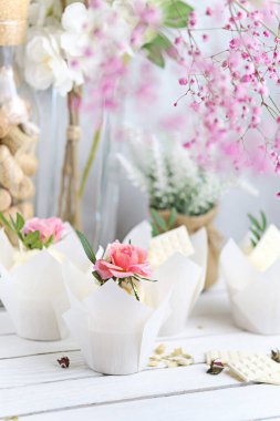 Beyaz tereyağı kremalı birkaç kek ve beyaz ahşap bir masada pembe bir gül. Sevgililer Günü ya da Anneler Günü hediyesi. Kırsal biçim.