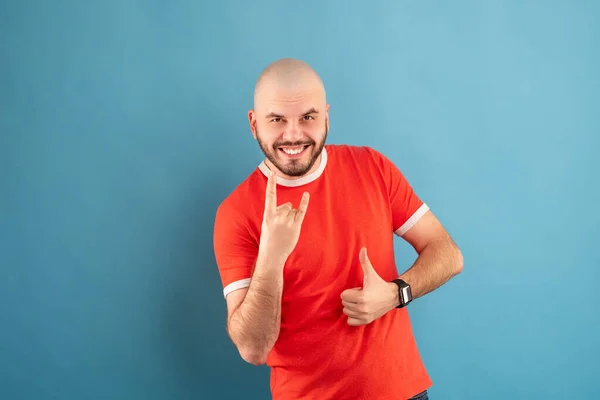 Ein Mann mittleren Alters mit Bart im blauen T-Shirt vor rotem Hintergrund steht jubelnd vor dem Sieg. Isoliert. — Stockfoto