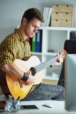 young man sitting on a table at the computer and playing guitar