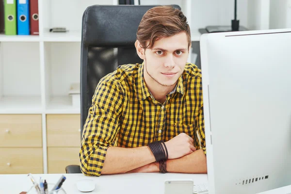 the young man behind the desk in the office working on the compu