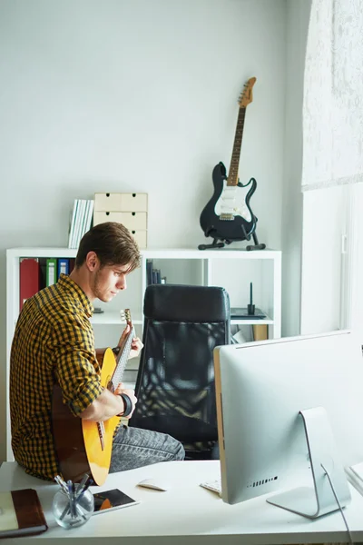 young man sitting on a table at the computer and playing guitar