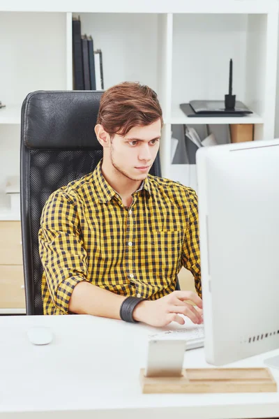 the young man behind the desk in the office working on the compu