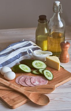 Salata için malzemeler. Salatalık, yumurta, peynir, jambon, sos, havlu, salata, tahta masada. Rustik.