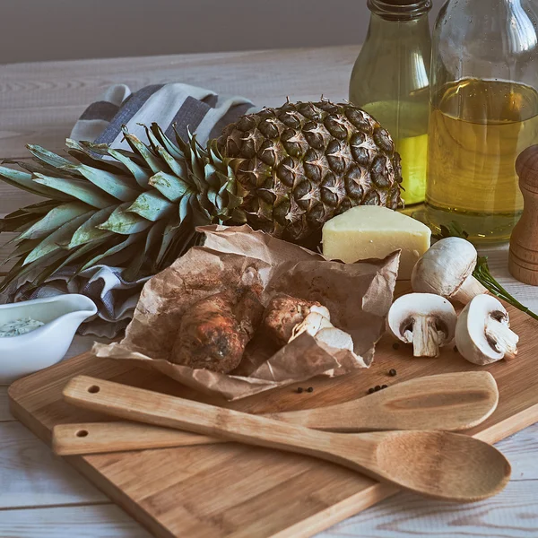 Ingredients for making pasta and pizza. Mushrooms, meat, pineapple, sauce, cheese, butter on the wooden table. Rustic.