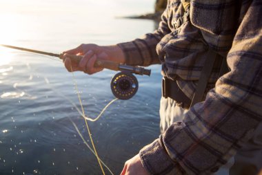 İngiliz Kolombiyası Vancouver 'da suda yürürken elinde olta ve makara tutan ekose gömlekli bir balıkçının yakın çekimi.