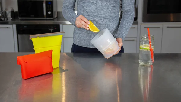 A women holds a clear a food-grade silicone bag with orange slices as part of a zero-waste lifestyle to replace plastic bags. Surrounded by other silicone products.