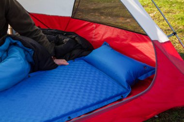 A man gets his tent and sleeping bag ready at a campground by inflating and setting up his blue blow-up mattress pad to put for under his sleeping bag clipart