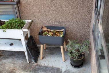 Fresh food and bedding material is added to an outdoor vermicomposter beside a planter. Worm composters are a perfect solution in an apartment, on a balcony or porch, or inside to process food waste clipart