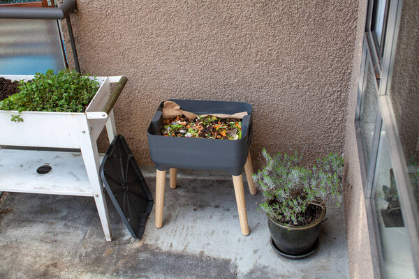 Fresh food and bedding material is added to an outdoor vermicomposter beside a planter. Worm composters are a perfect solution in an apartment, on a balcony or porch, or inside to process food waste