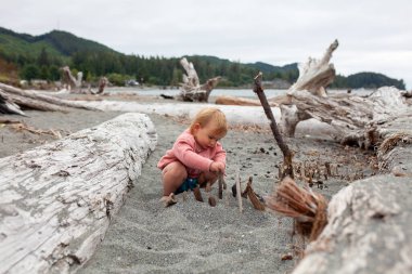 Bir çocuk bulutlu bir günde kumlu bir plajda oynuyor. Plaj günleri, çocukların çevrelerine uyum sağlamaları için yapılandırılmamış önemli oyun fırsatları sunar..