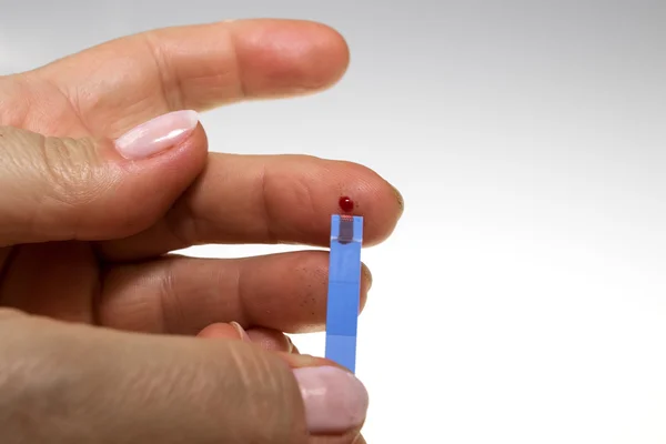 Diabetic places a drop of blood on a test strip — ストック写真