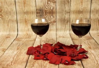 Two glasses of red wine, rose petals and Valentine hearts on woo