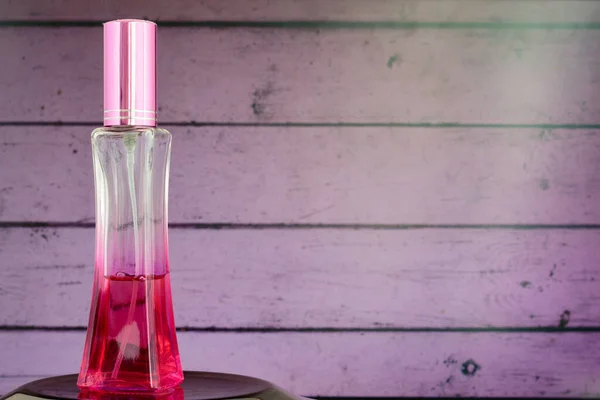 Pembe ahşap arka planda güzel bir şişede kadın parfümü..
