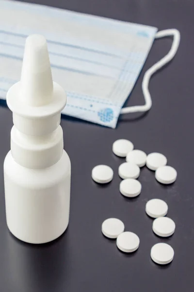 Large unnamed nasal spray with medical mask and pills on a dark background.