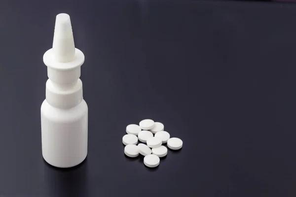 Geniş, isimsiz bir burun spreyi ve koyu bir arka planda haplar..