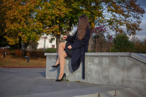 Das Mädchen sitzt im Park. Ein Mädchen im Mantel ruht auf der Straße. Spaziergang an einem Herbsttag. — Stockfoto