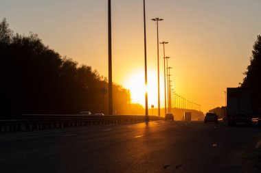 Otoyolda gün batımı. Güneş otoyolun üzerinde batıyor. Yüklü otoyol. Arabalar akşamları şehirden yola çıkar..