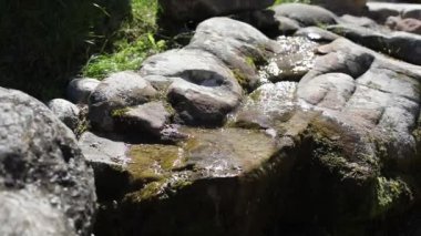 Taşların üzerinden su akıyor. Alp kaydırağındaki taşların arasında bir dere. Bahçede peyzaj. Çakıl taşları arasında su akıntısı.