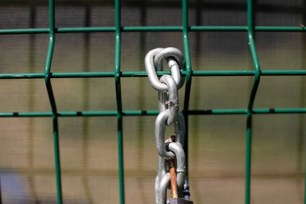 Chain on the fence. A metal chain hangs on the fence. Fence enclosing the territory with a lock and chain for blocking.