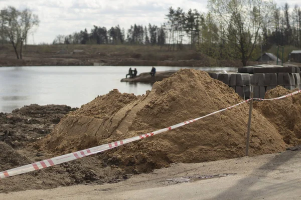 Mountains of sand at a construction site. Construction site near the lake. Creation of an embankment in the park. Preparation of construction works by the lake. Site construction.