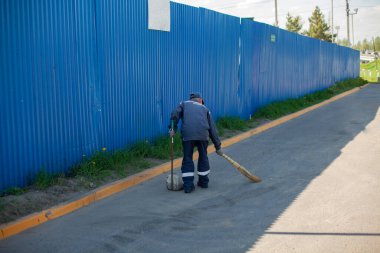 Yol temizleyicisi. Hademe bir süpürgeyle bölgeyi tarıyor. Yoldaki çöpleri temizliyorum. Çitin yanındaki işleri düzene sokuyorum. Otoparkta temizlik yapıyordum. Temizlikçi çalışıyor..
