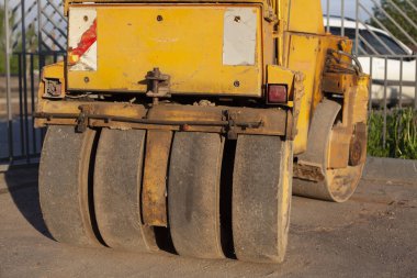 Sarı asfaltı asfaltlamak için buldozer. Yol tamiri için ağır makineler. Otoparkta çalışan bir araba. Yaşlı istifçi hareketsiz duruyor..