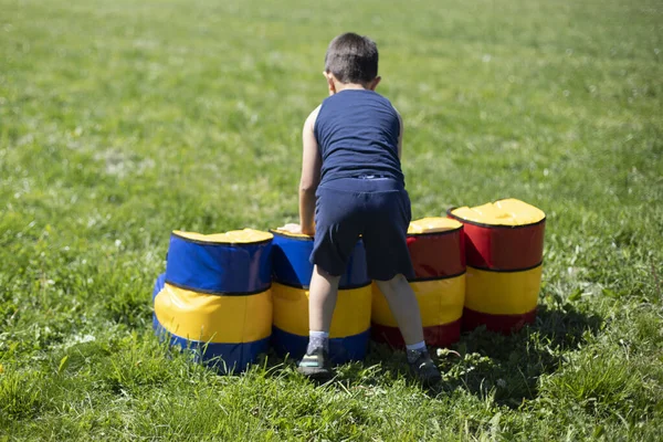 子供は障害物コースを克服します 夏の子供の遊び 新鮮な空気中の少年の残りの部分 子供は緑の芝生で遊んでいる プレーのためのスポーツソフトバリア — ストック写真