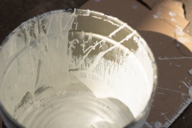 Bir kova beyaz boya. Boya lekeli konteynır. Avludaki onarımların detayları.