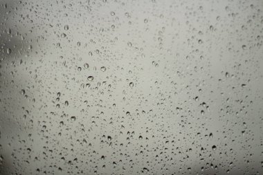 Camdaki yağmur damlaları. Pencerenin dışında nemli hava var. Şeffaf bir yüzeyde damlaların dokusu. Kötü bir gün..