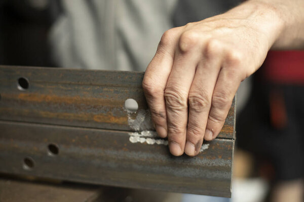 Drilled holes in the metal. Work in a metal workshop. The hand holds a steel blank. A man works in the garage.