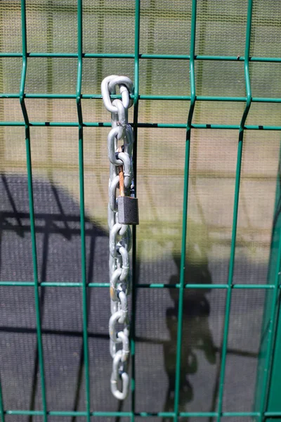 Chain on the fence. A metal chain hangs on the fence. Fence enclosing the territory with a lock and chain for blocking.