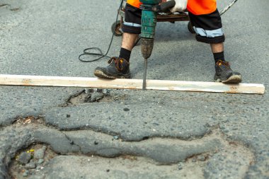 Asfaltı bir kaya matkabıyla kaldırıyor. Yoldaki asfalt tabakasını kaldırıyorum. İşçi bir kaya matkabı tutuyor. Yol tamiri. Elektrikli çekiç kullanarak..