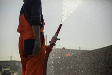 Bir adam hortumdan su döker. Yangın musluğundan akan bir çeşme. Yolu suluyorum..