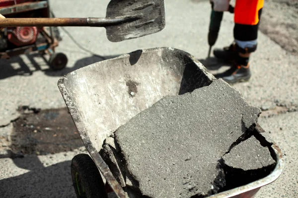 Construction waste trolley. Puts the asphalt into the cart with a shovel. A worker is laying asphalt. Road repair. Destruction of old asphalt.