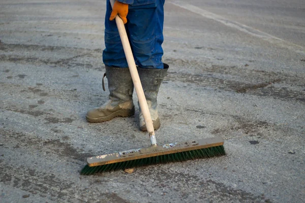 Cleaning the dirt out of the way. A man in boots cleans the surface of the debris. Urgent cleaning on the street. A large mop in the hands of a worker.