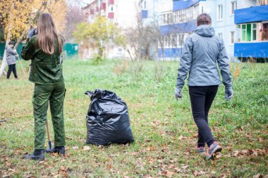 Sonbaharda yaprak toplamak. İnsanlar sokakları temizliyor. Bahçeyle ilgilenen bir bahçıvan. Kuru yapraklar poşetlerde toplanır. Evin yakınındaki güzellik merkezinde..