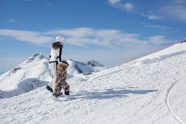 妈妈带着孩子在滑雪胜地 一家人穿着特殊的滑雪装备在雪地里散步 在雪地的斜坡上休息 一个女孩带领一个孩子学会在雪地里从山上骑马 多霜的阳光灿烂的山区 — 图库照片
