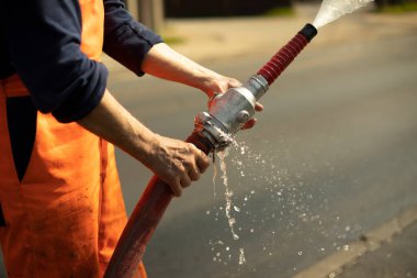 Su hortumu. Borudan gelen su akışı. Adamın biri elinde yangın hortumu tutuyor..