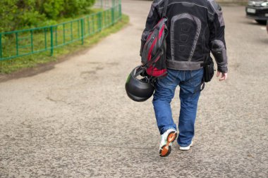 Elinde kask olan bir motosikletçi. Motosikletli caddede yürür. Arkadaki adam..