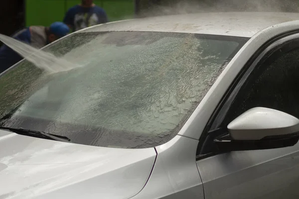 Car wash. The car is washed under the pressure of a jet of water. Using a water spray to wash off dirt from the surface of the car.