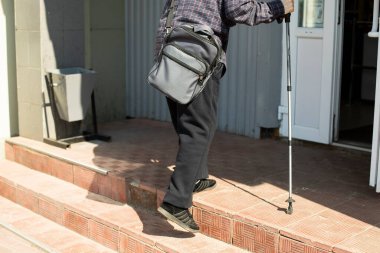 Destek çubuğu olan bir adam. Yaşlı adam basamakları tırmanır. Binaya bir adam giriyor..