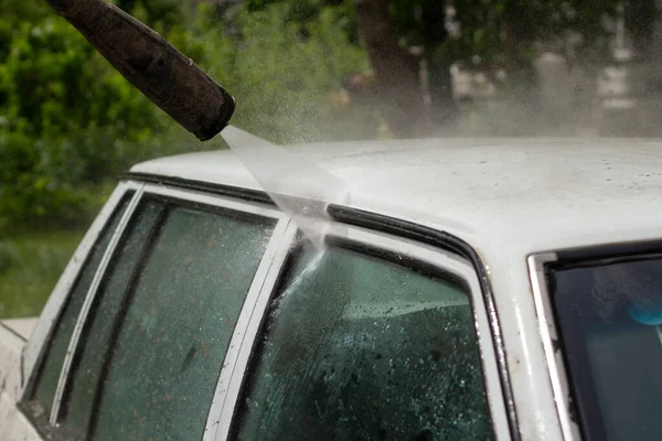 車の屋根を洗う ホースから車への水の流れ 白い車は電気機器を使って洗浄されます — ストック写真