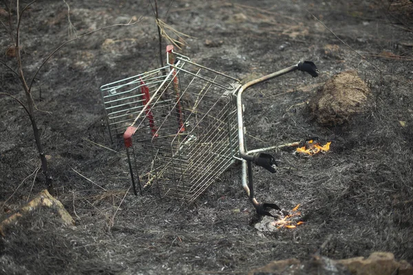 The supermarket cart is on fire. A grocery basket caught fire in the street. The steel basket is covered with fire.