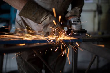 İş öğütme makinesi. Sürtünmeden kaynaklanan kıvılcımlar. Atölyedeki bir adam metali işliyor. Çelik bir parçanın oluşturulması.
