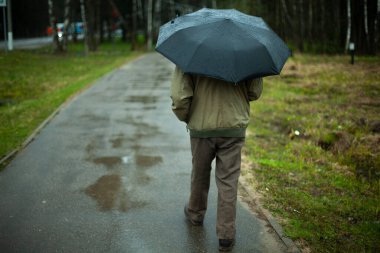 Şemsiyeli bir adam caddede yürüyor. Yağmurlu sonbahar havası. Vatandaş siyah bir şemsiye altında hafif yağmurdan saklanıyor. Bir adam şehirde yürüyor..