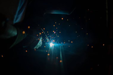 Metal kaynaktan ateş. Kaynak makinesiyle çalışırken karanlıkta kıvılcımlar saçar. Yüksek sıcaklıkta çalış. Garajda bir adam çelik bir dikiş onarıyor..